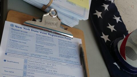 Voter registration forms and clipboard on a table with an American flag
