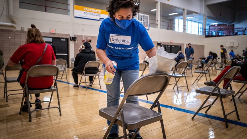 Staff member cleaning chairs in a large hall set up for vaccinations