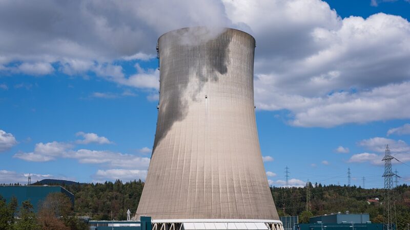 Large nuclear power plant cooling tower releasing steam under a blue sky